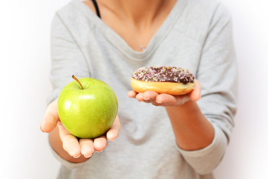 Healthy lifestyle or nutrition concept with young woman holding in hands an green apple and a donut