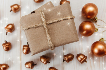 Christmas composition.Present box with twine and craft paper,golden acorns and balls.White wooden table.