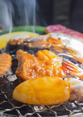 Selective focus of grilled items includes squid pork beef shrimp and vegetable with smoke on burned charcoal over the dark background