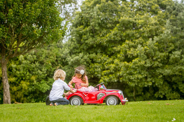 young happy children - boy and girl - driving a toy car outdoors