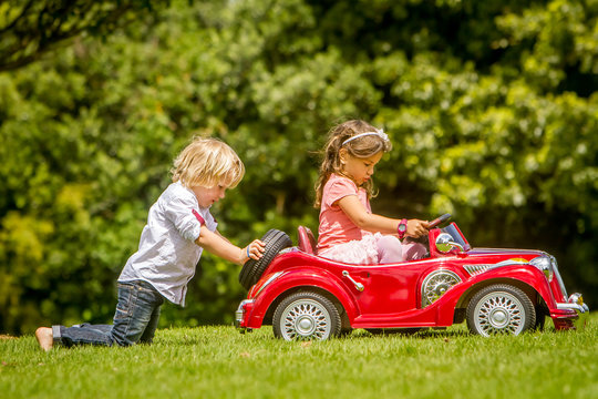 Young Happy Children - Boy And Girl - Driving A Toy Car Outdoors