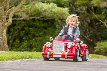 young happy child boy driving a toy car outdoors in park