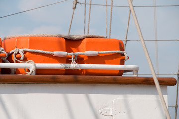 Bright orange lifebuoy on a deck yacht side. Blue sky background