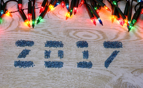 Figures 2017 from glass beads on the white wooden background and garland big lights on top frame New Year and Christmas template copyspace card concept for price and description winter sale item.