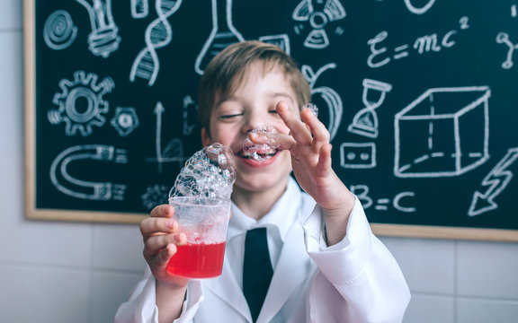Portrait of happy little boy holding glass with soap foam against of blackboard with drawings