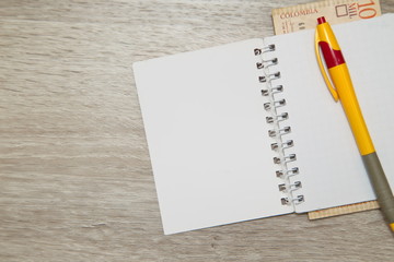 Blank notebook page and pen with Colombian pesos on wood office table