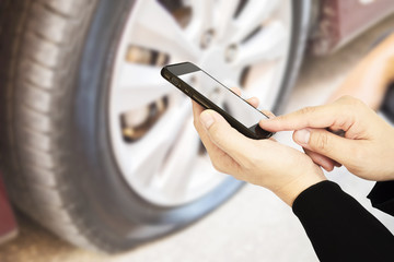 Man is using mobile phone to call someone over blurred technician is repairing car flat tire