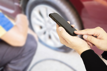 Man is using mobile phone to call someone over blurred technician is repairing car flat tire
