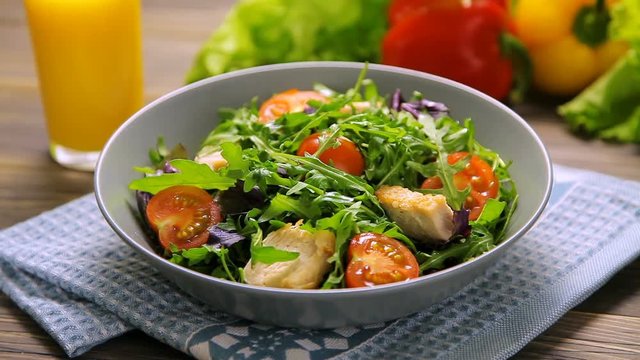 Fresh salad with chicken, tomatoes, arugula, mesclun, basil and orange juice on a cloth napkin, on wooden table