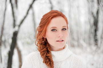 Ginger cute girl in white sweater in winter forest. Snow december in park. Christmas time. Happy New Year poster with beautiful woman.