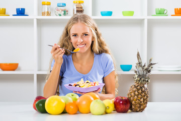 Beautiful girl enjoys eating fruit salad at her home.
