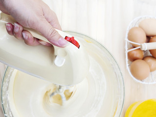 Toy view of lady's hand preparing cake using hand mixing machine with egg and butter