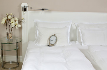 White bedhead with pillows, bedclothes and alarm clock showing half past seven