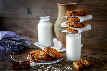 Homemade oatmeal cookies with nuts and raisins and glass of milk on dark wooden background, closeup, selective focus
