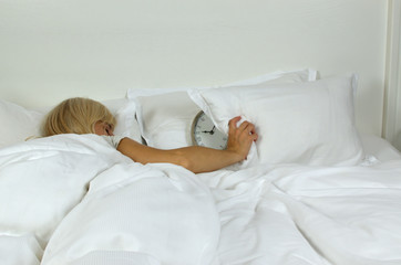 Sleeping woman covering alarm clock with pillow which is showing she overslept the time