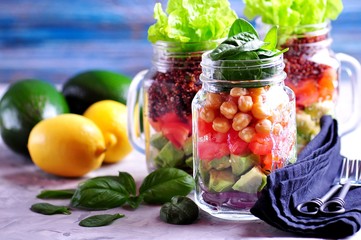 Healthy salad with quinoa and chickpeas, avocado, tomato, red onion, baby spinach, lettuce, olive oil in a Mason jars.