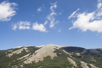 Das karstige Bergmassiv des Monte Cervati unter einem blauen Himmel mit weissen Wolken im Hinterland des Cilento, Italien