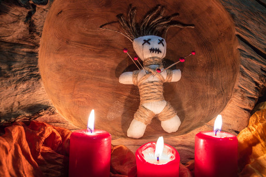 A voodoo doll with needles stands on an altar with candles
