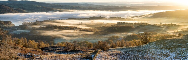 Obraz premium Vibrant golden sunlight shining over hills covered in Autumnal mist in the Lake District.