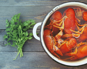 Boiled crayfish in a pan, greens of parsley and a knife on a wooden surface of a table, top view