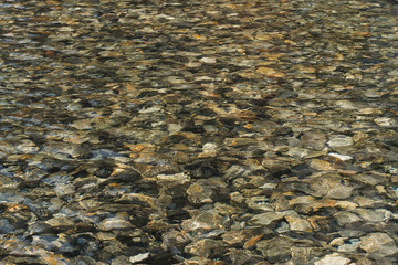 Rocks at the bottom of a clear mountain stream. Ripples creating shadows onto round pebbles in water.