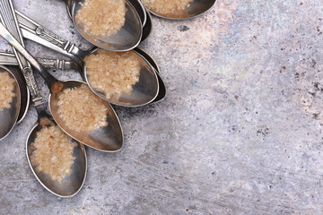 Silver spoonfuls with brown sugar on metal table top view