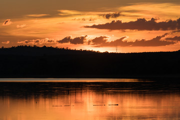Obraz premium Beautiful orange sky dark clouds at sunset reflection on the lake water with silluette of mountain. Sunset on a lake for background, thailand 