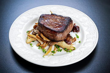 Tasty Beef Mignon steak with mushrooms and herbs on plate.