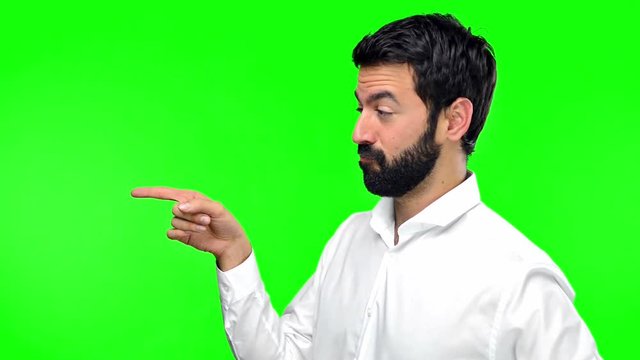 Handsome man pointing to the lateral on green screen chroma key