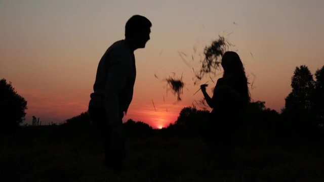 A boy and a girl couple silhouette hugging, playing, kissing during sunset