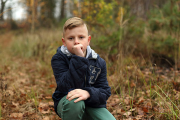 Śliczny chłopiec, nastolatek kuca w lesie na polanie. - obrazy, fototapety, plakaty