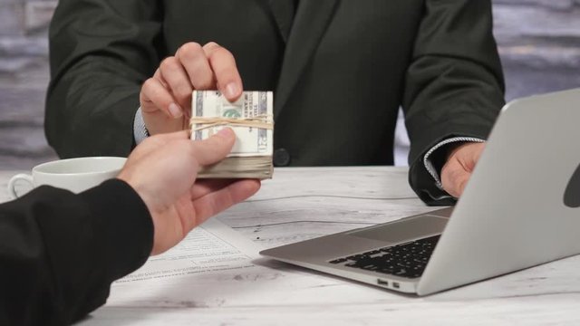 Man working on a computer taking bribe cash money from another person.