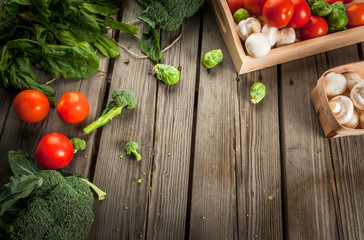 Fresh raw organic vegetables on a rustic wooden table in basket: spinach, broccoli, Brussels sprouts, tomatoes, mushrooms, champignons. 