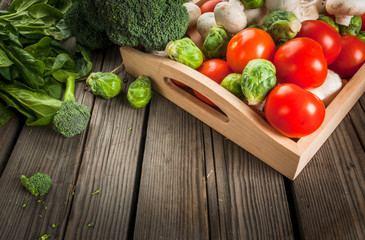 Fresh raw organic vegetables on a rustic wooden table in basket: spinach, broccoli, Brussels sprouts, tomatoes, mushrooms, champignons. 