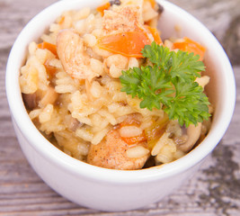 Risotto with chicken, bell pepper, onion, portobello and parsley on a wooden background