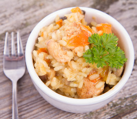 Risotto with chicken, bell pepper, onion, portobello and parsley on a wooden background