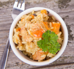 Risotto with chicken, bell pepper, onion, portobello and parsley on a wooden background
