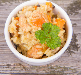 Risotto with chicken, bell pepper, onion, portobello and parsley on a wooden background