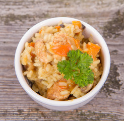 Risotto with chicken, bell pepper, onion, portobello and parsley on a wooden background