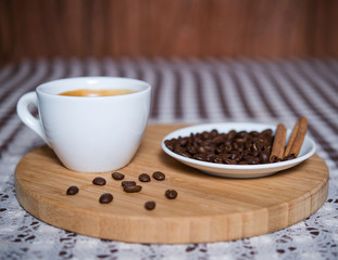 cup of coffee and coffee beans with cinnamon on a wooden tablet
