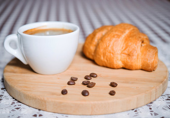 cup of coffee with a croissant on a wooden tablet
