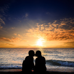 Kissing man and woman sit on the seashore next to the surf zone