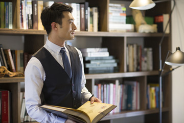 Young businessman reading book in his study