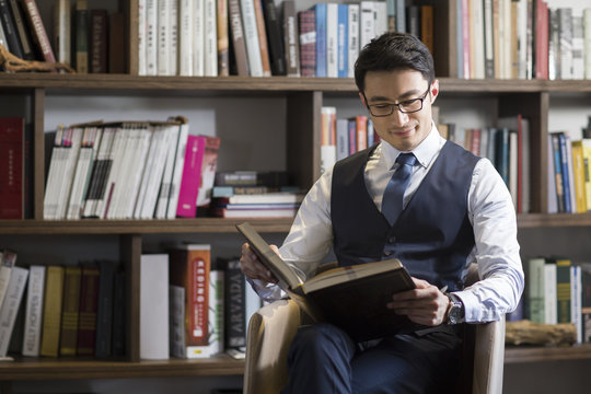 Young businessman reading book in his study