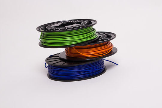 Top view of blue, orange and green 3D printer filament spools stacked off-center 