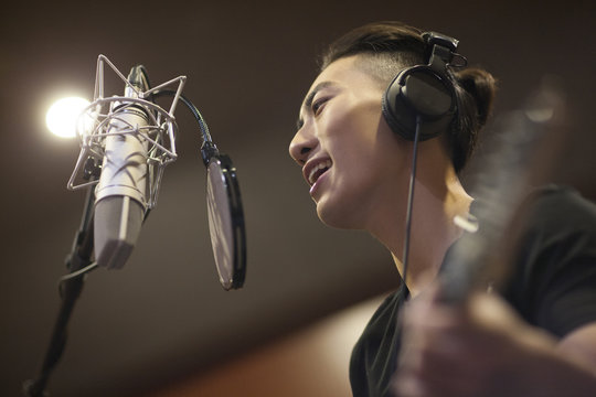 Young man singing with guitar in recording studio
