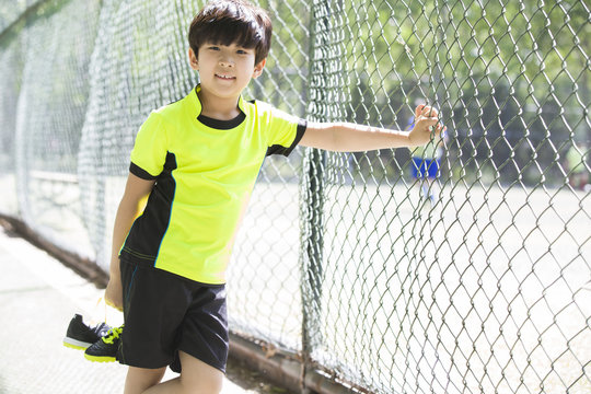 Happy boy in sportswear leaning against chainlink fence