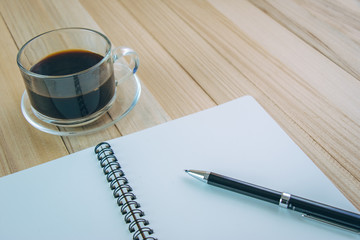 Put pen on blank notebook near glass of hot coffee
