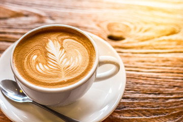 cup of the latte art coffee with spoon and plate on the brown bark beautiful texture background with warm light