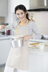 Cheerful young woman cooking in kitchen